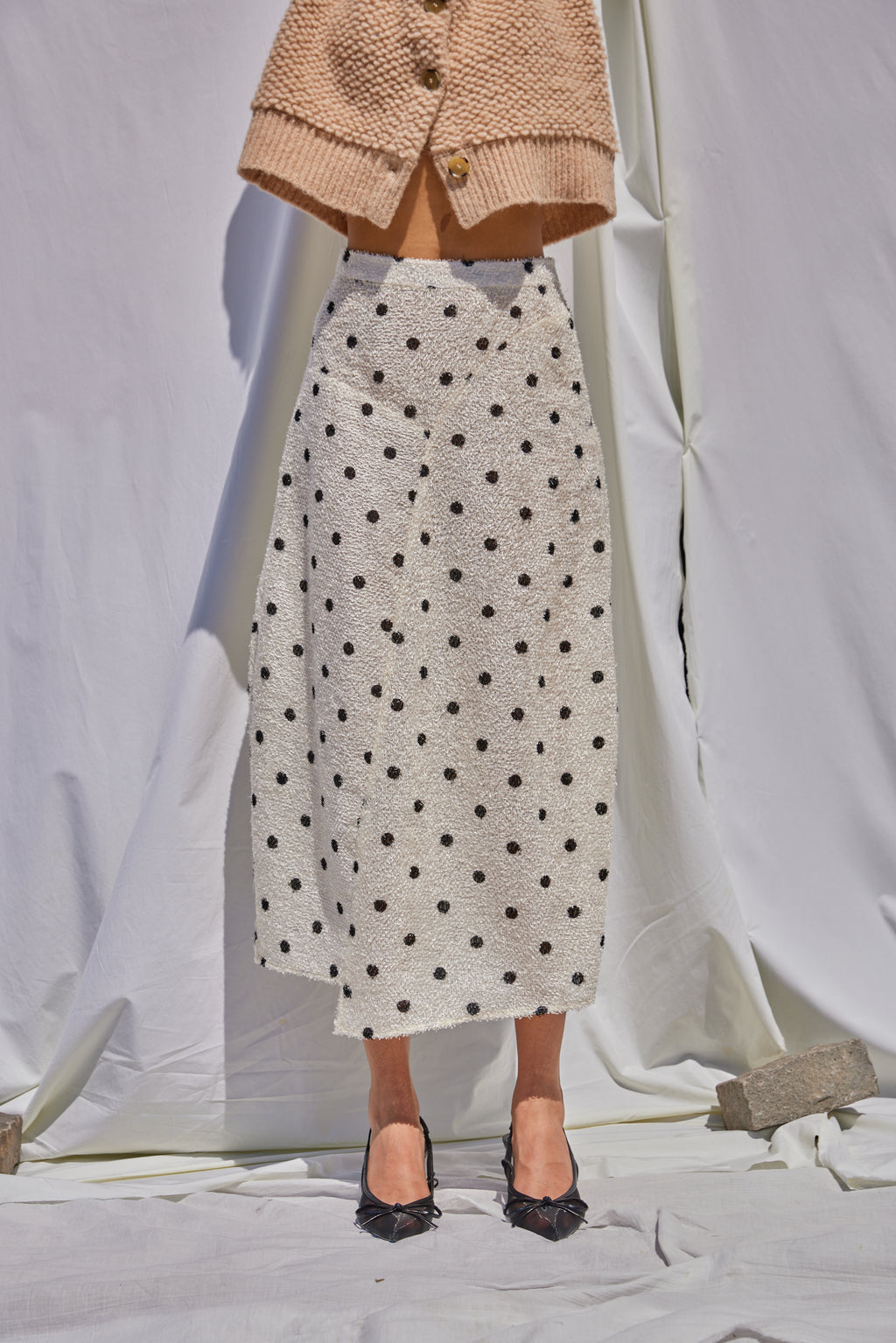Mannequin wearing a beige cardigan, polka dot skirt, and black shoes on a white background