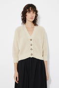Woman wearing a beige Sclater knitted cardigan by Rita Row with buttons on a white background