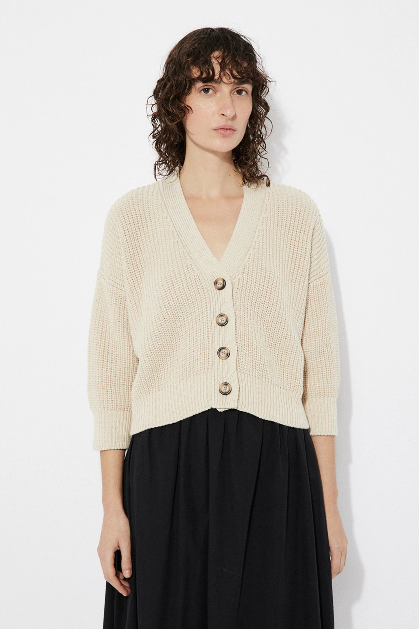 Woman wearing a beige Sclater knitted cardigan by Rita Row with buttons on a white background