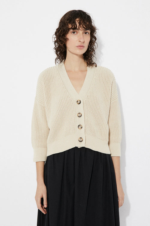 Woman wearing a beige Sclater knitted cardigan by Rita Row with buttons on a white background
