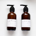 Two brown bottles with pump dispensers labeled 'Driftwood' and 'Wild Flower' on a white background.