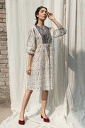 Woman in a floral dress standing in front of a white curtain with a brick wall background