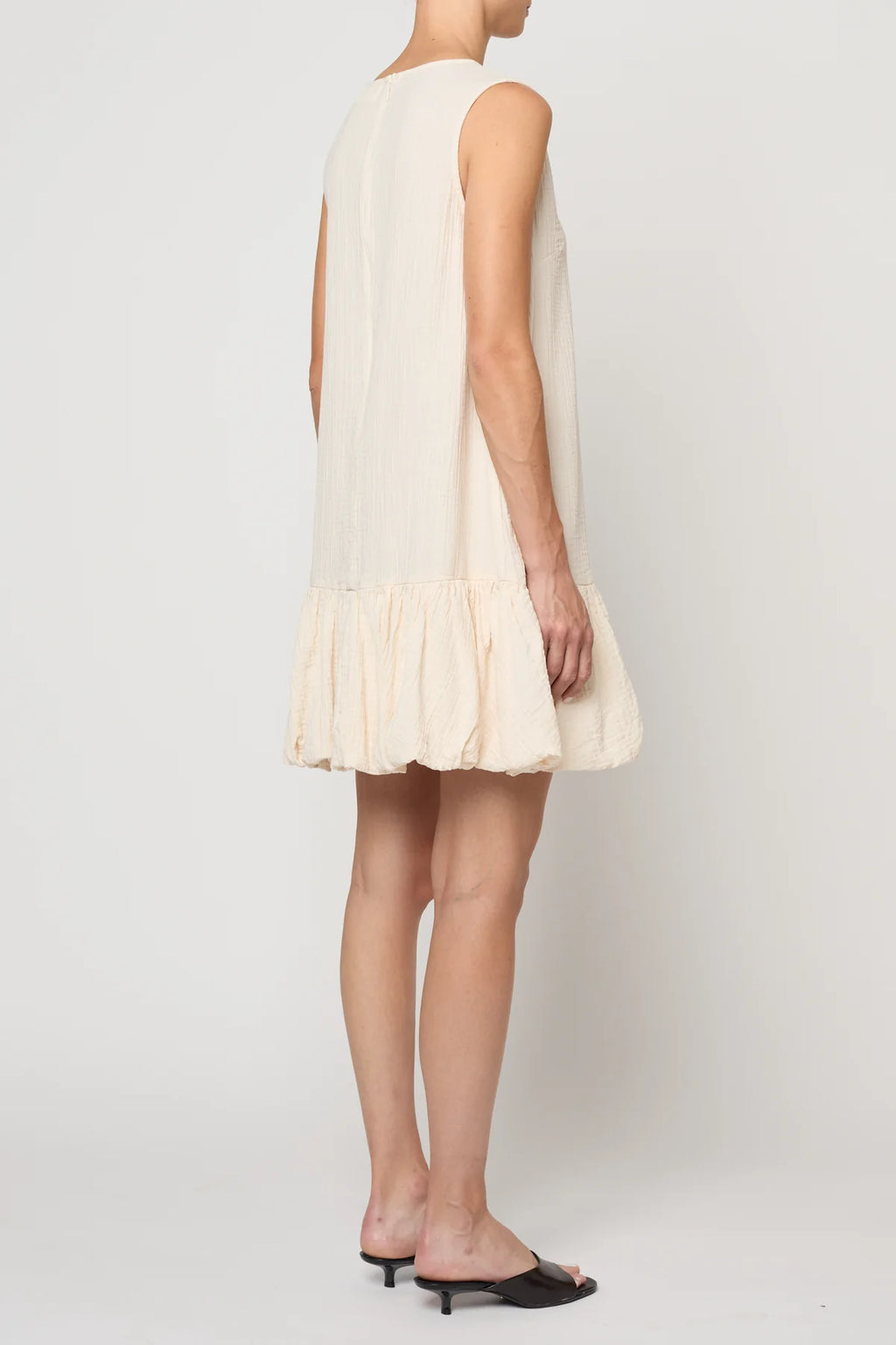 Woman wearing a cream-colored dress by Atelier Delphine with a plain background