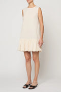 Woman wearing a cream-colored dress by Atelier Delphine with a plain background