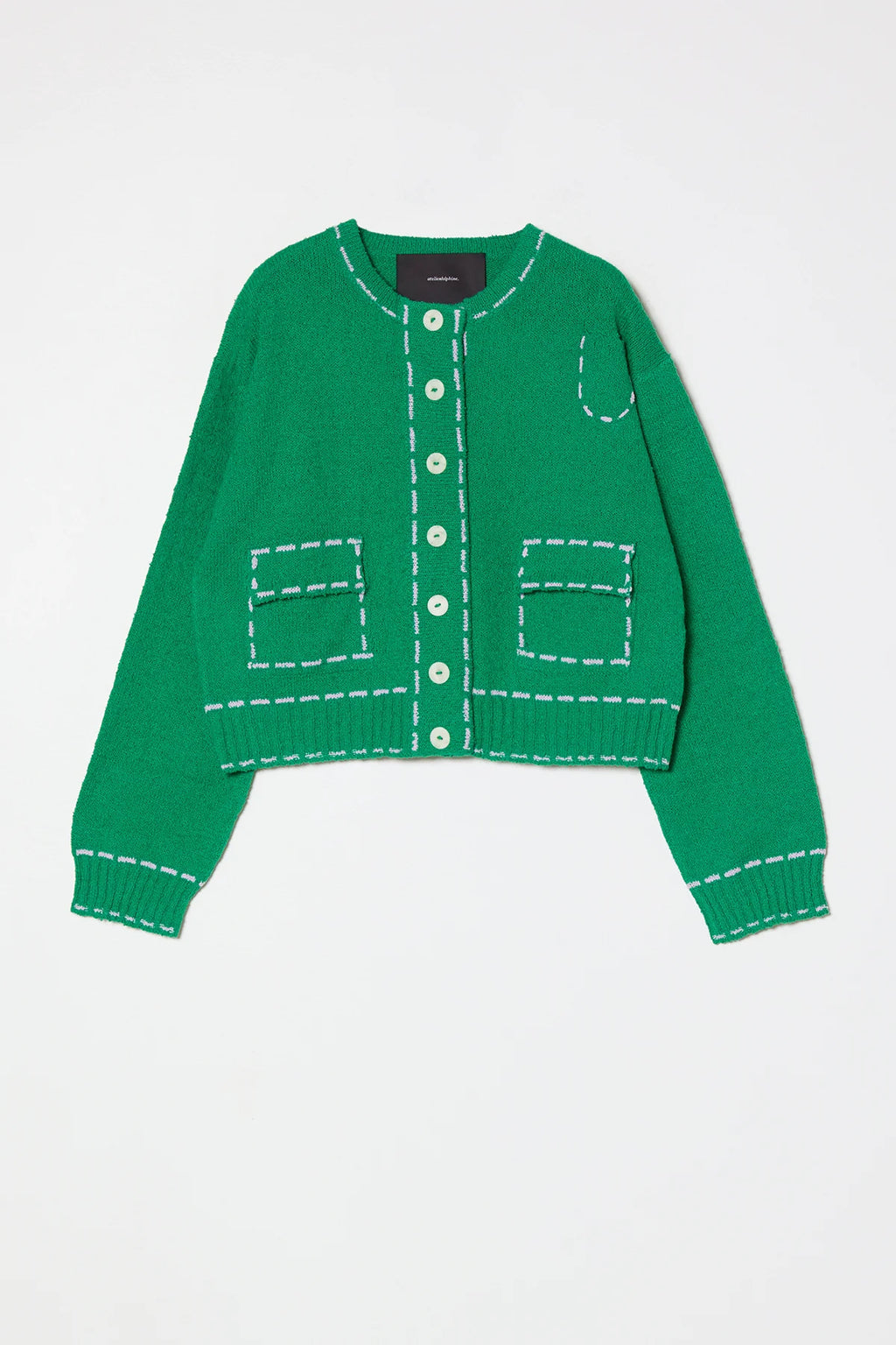 Woman wearing a green sweater jacket with lilac stitching by Atelier Delphine and a white skirt on a plain background