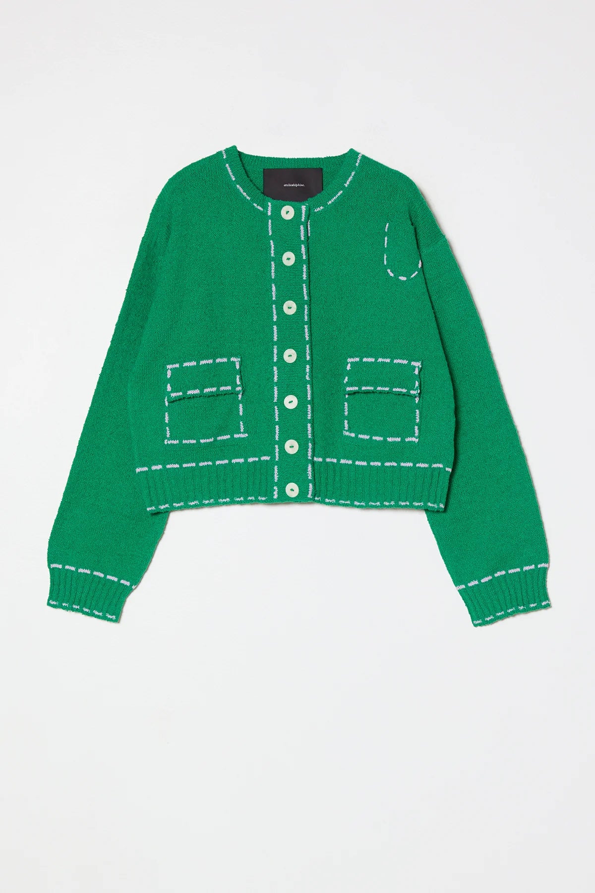 Woman wearing a green sweater jacket with lilac stitching by Atelier Delphine and a white skirt on a plain background