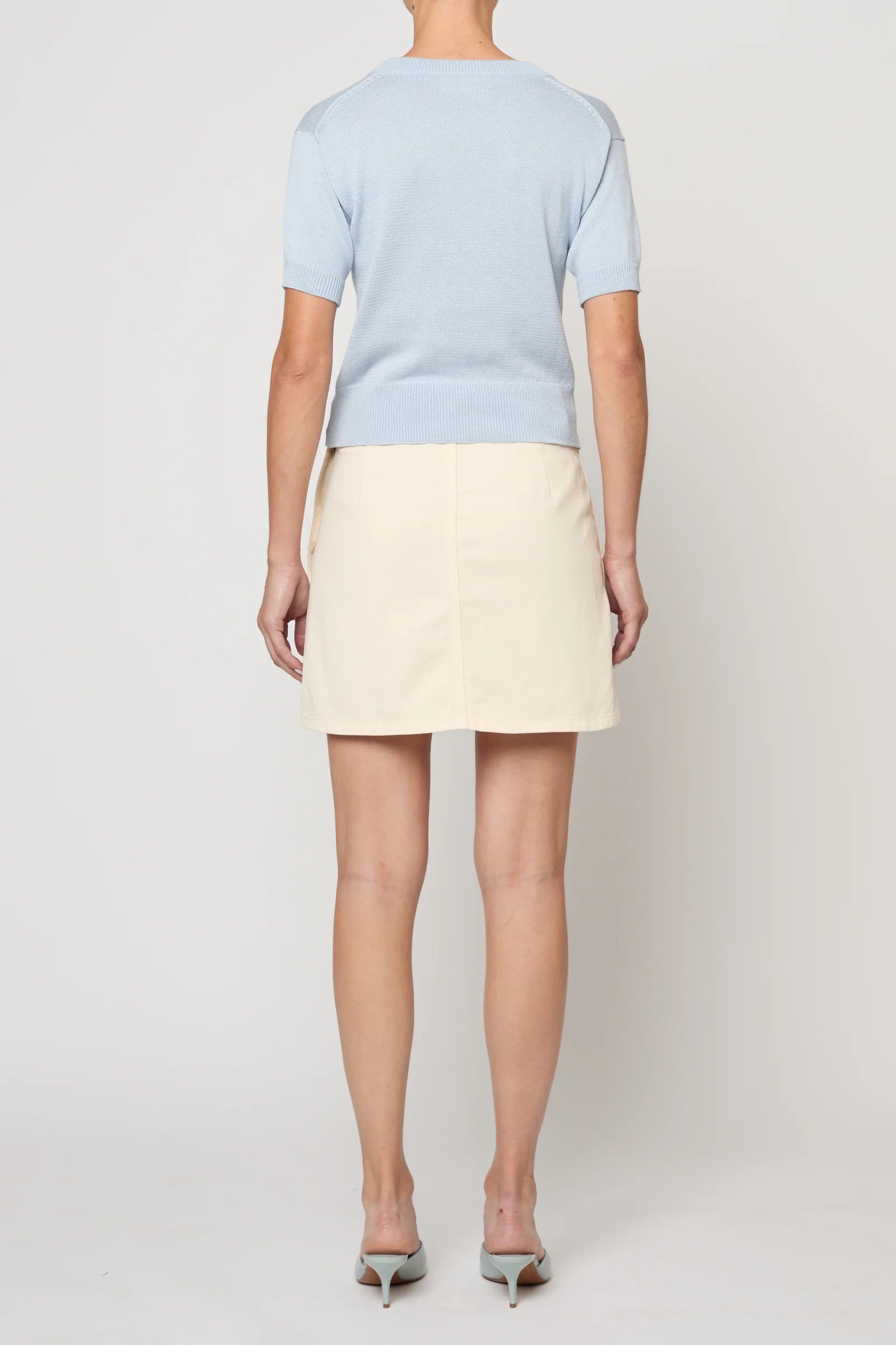 Woman wearing Pastel Blue Mari Top by Atelier Delphine and a cream skirt on a white background