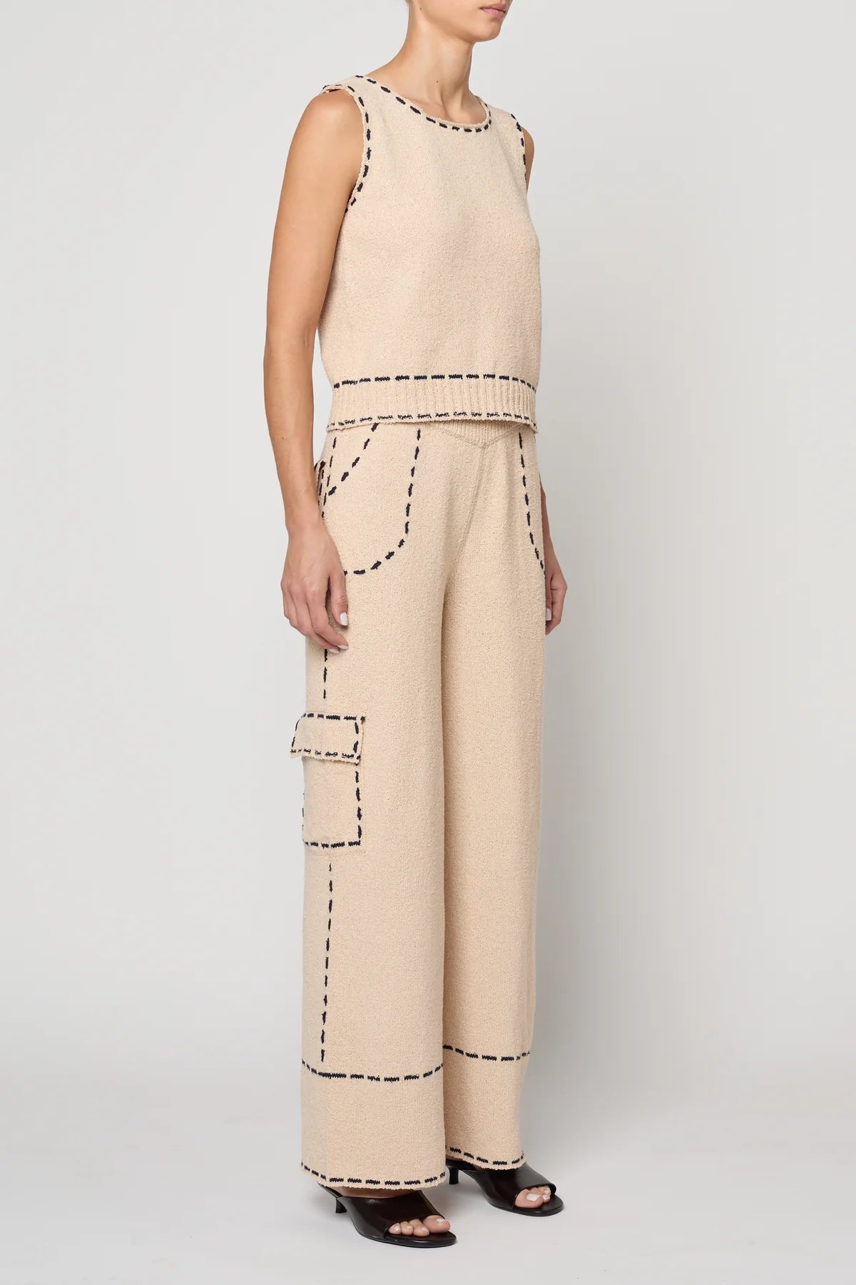 Woman wearing a beige sleeveless top with navy stitching by Atelier Delphine and matching pants