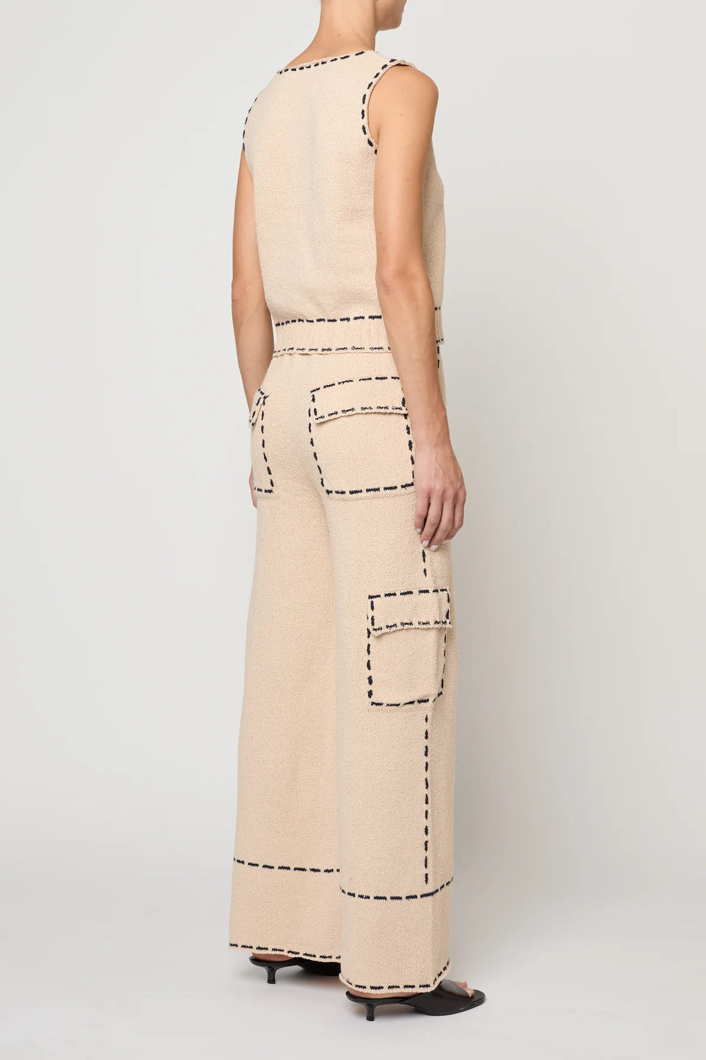 Woman wearing a beige sleeveless top with navy stitching by Atelier Delphine and matching pants