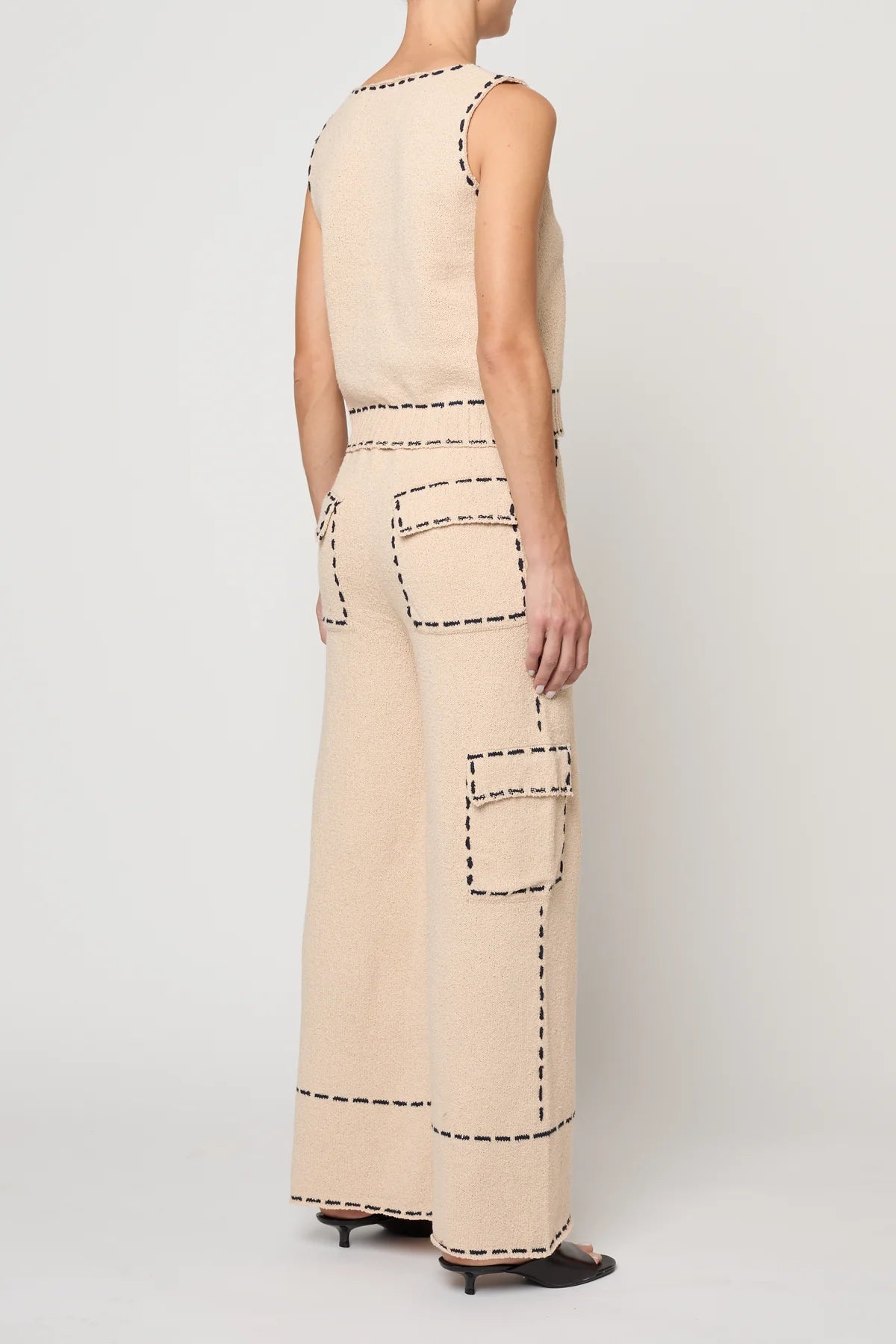 Woman wearing a beige sleeveless top with navy stitching by Atelier Delphine and matching pants