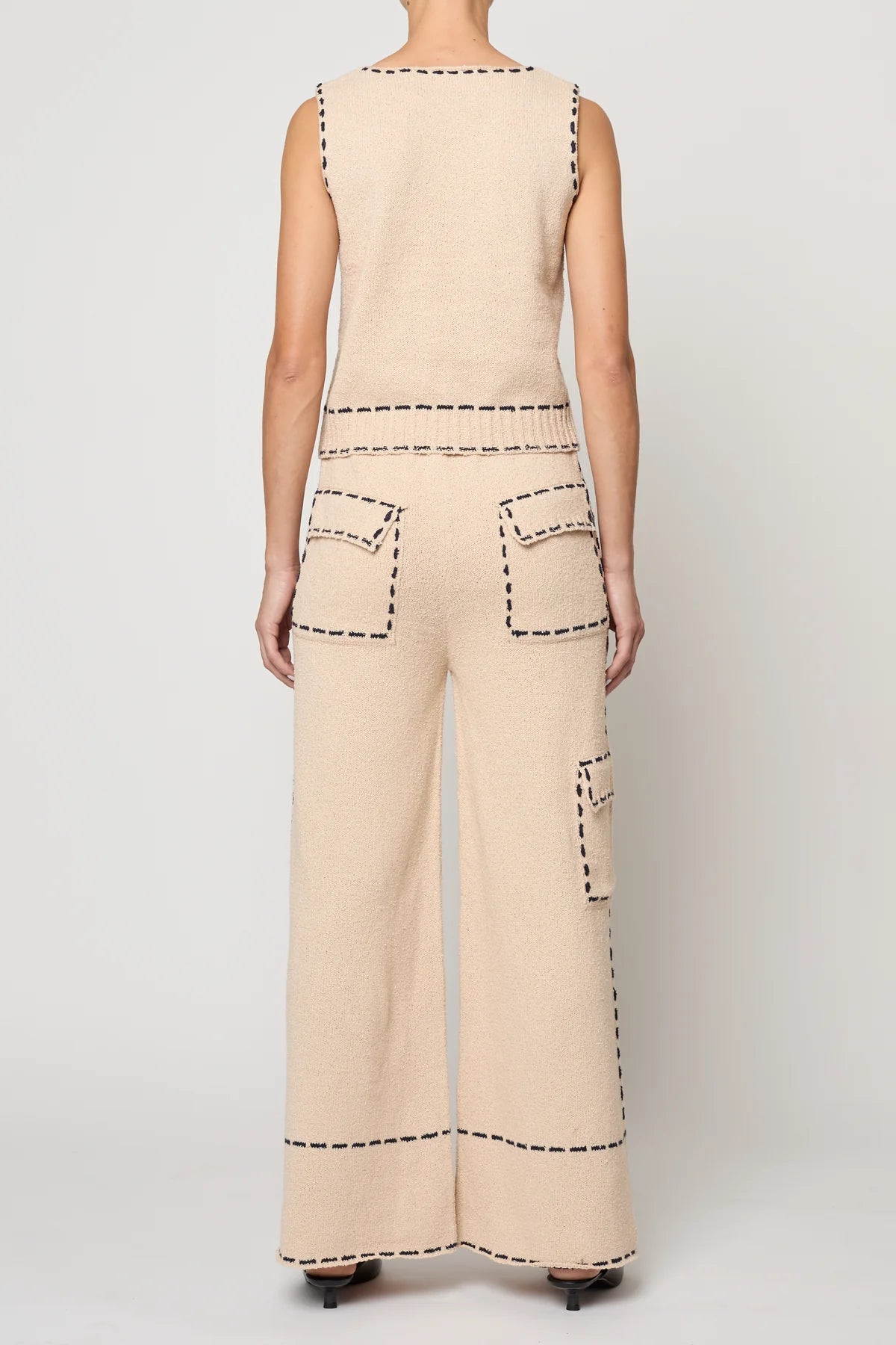 Woman wearing a beige sleeveless top with navy stitching by Atelier Delphine and matching pants