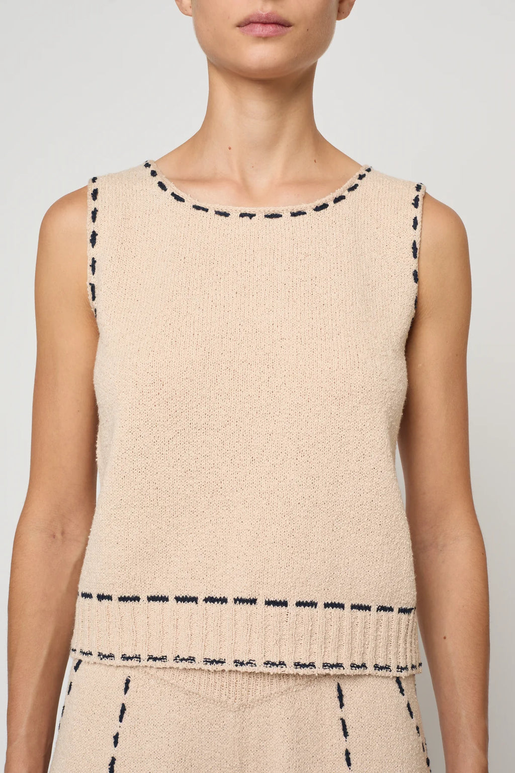 Woman wearing a beige sleeveless top with navy stitching by Atelier Delphine and matching pants