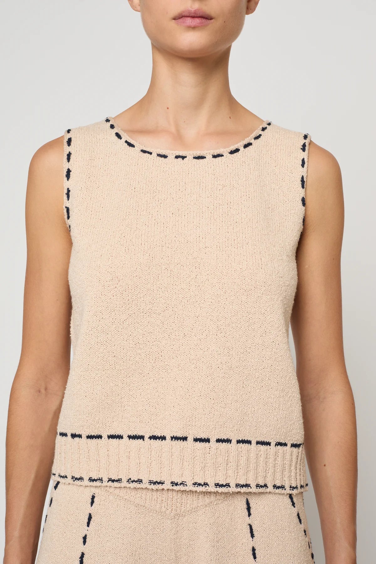Woman wearing a beige sleeveless top with navy stitching by Atelier Delphine and matching pants