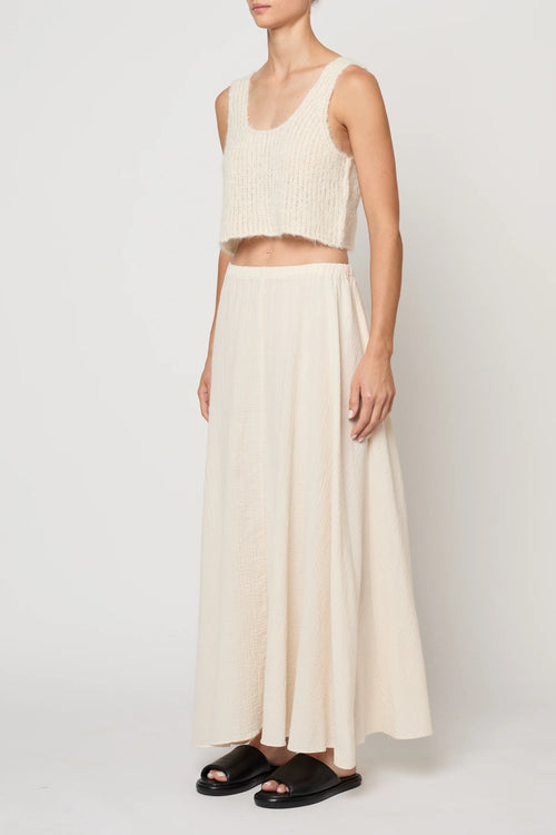 Woman wearing a cream knit tank by Atelier Delphine and a cream skirt