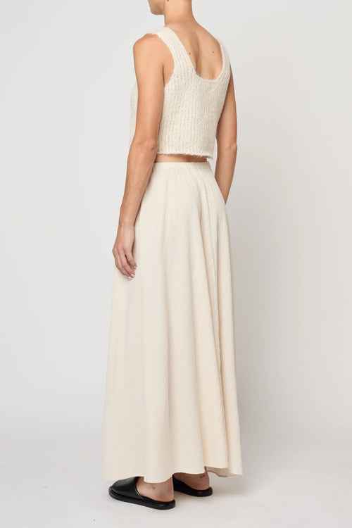 Woman wearing a cream knit tank by Atelier Delphine and a cream skirt