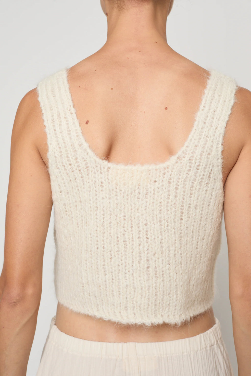 Woman wearing a cream knit tank by Atelier Delphine and a cream skirt