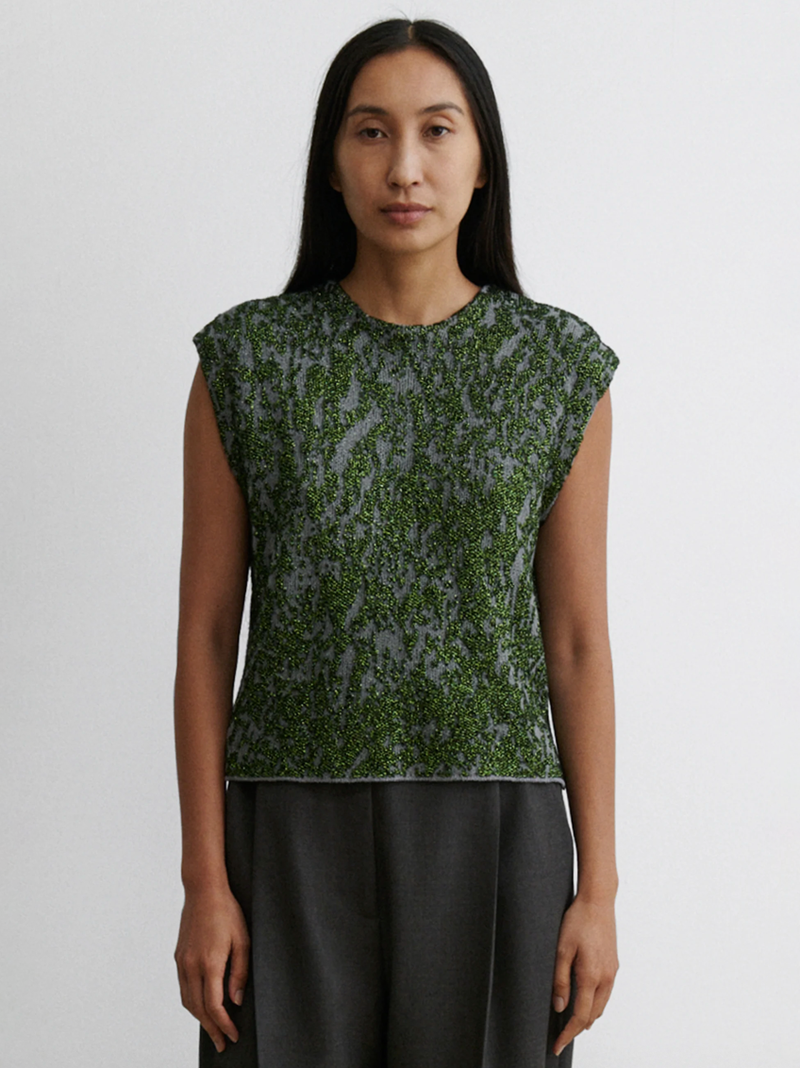 Woman wearing a green patterned top and black pants on a white background