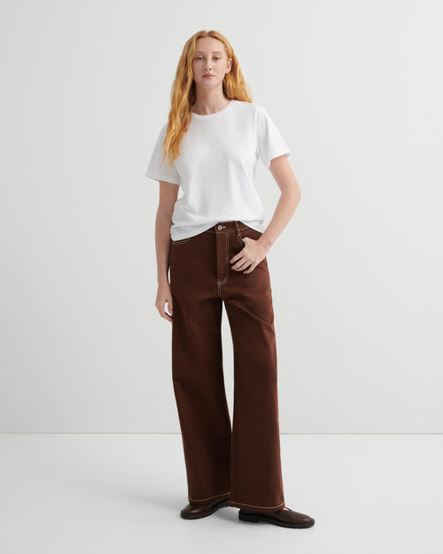 Woman wearing brown craft jeans by kowtow with a white shirt on a white background.