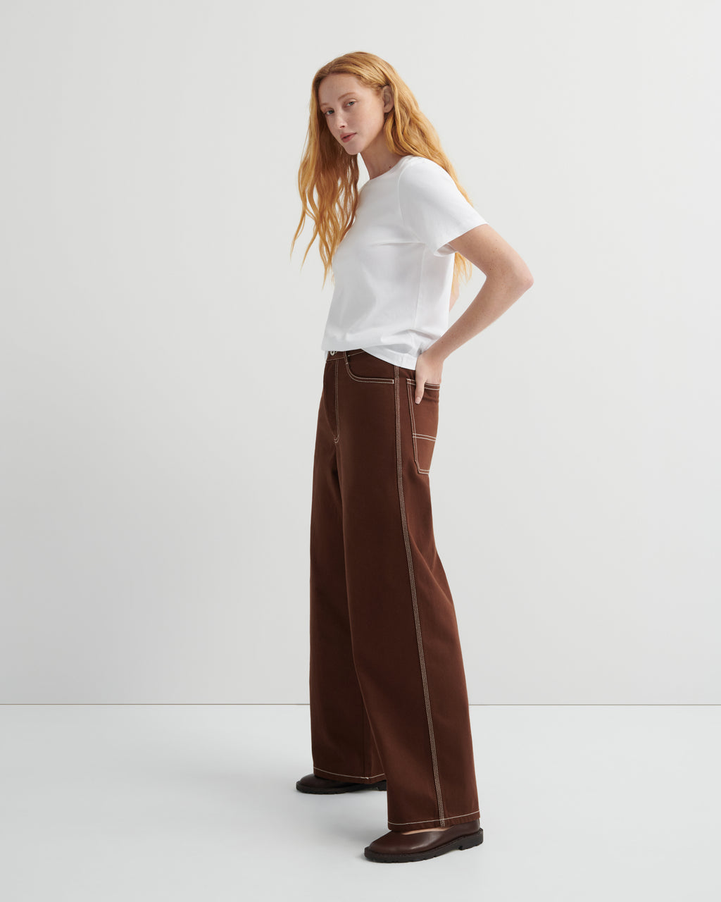 Woman wearing brown craft jeans by kowtow with a white shirt on a white background.