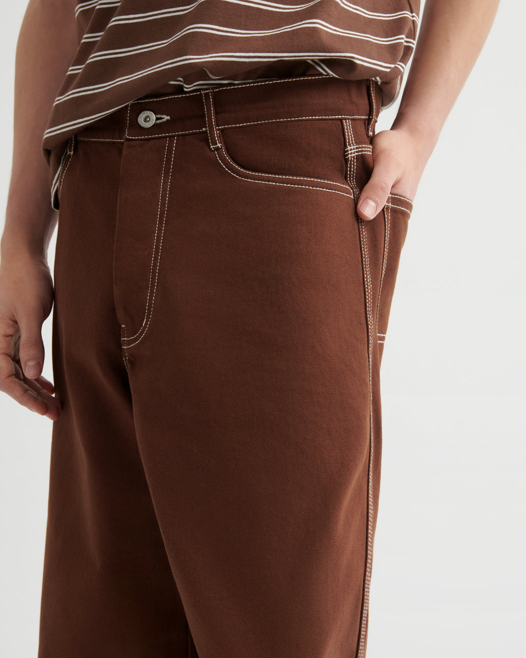 Woman wearing brown craft jeans by kowtow on a white background.