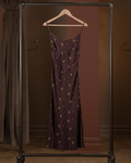 Purple dress with gold patterns on a hanger against a brown background