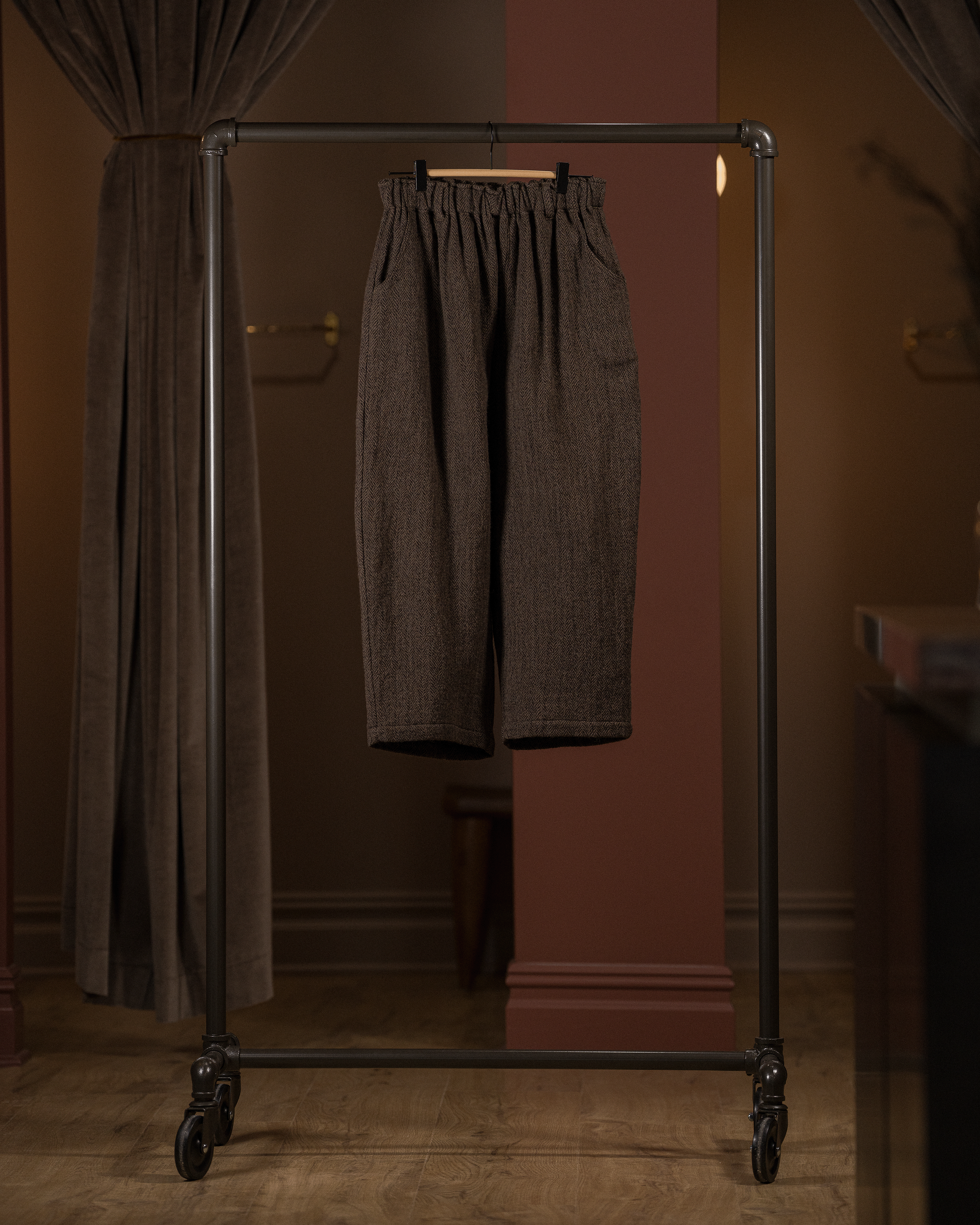 Brown pants hanging on a clothing rack against a brown wall.