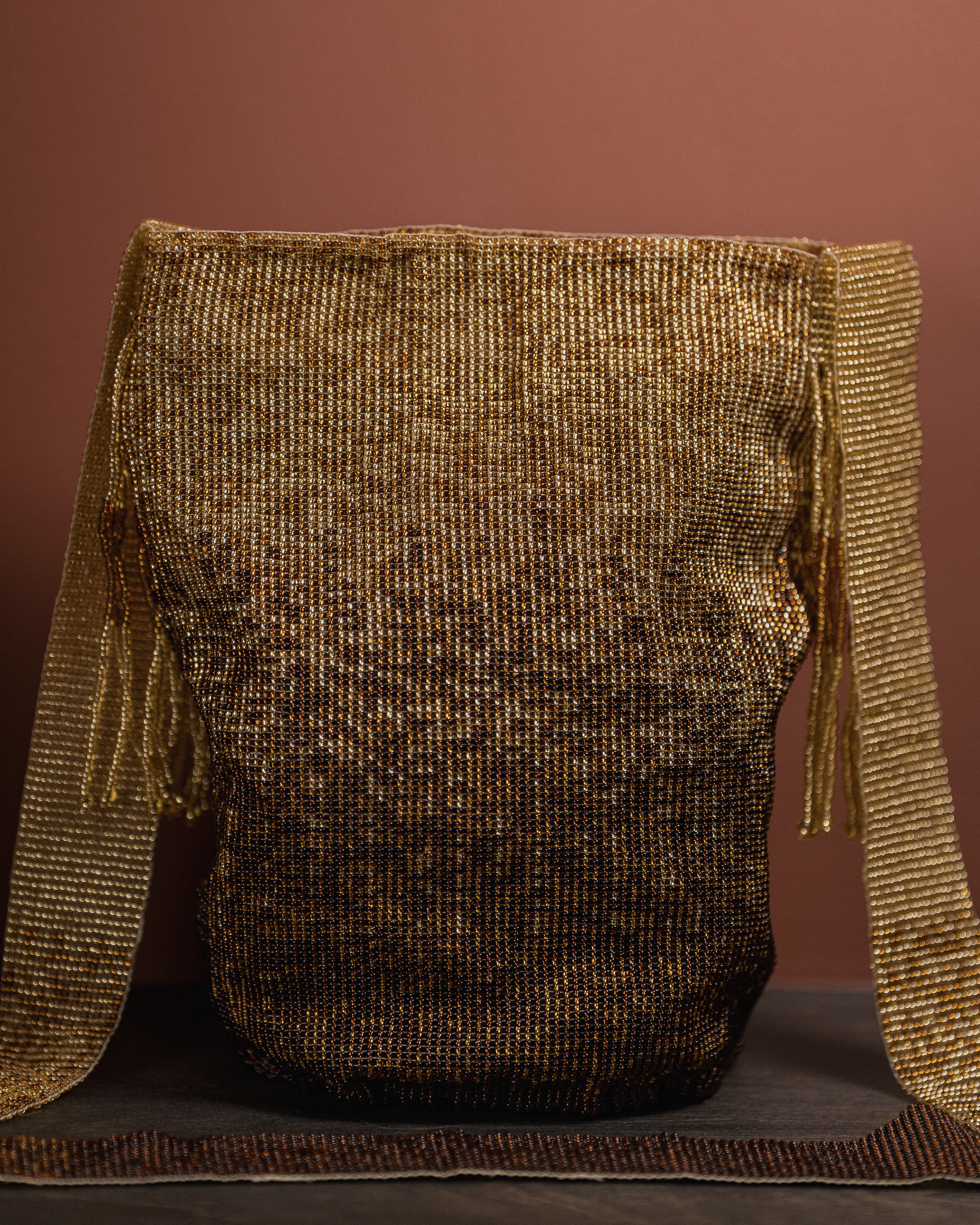 Textured brown bag with gold fringe on a dark surface against a brown background
