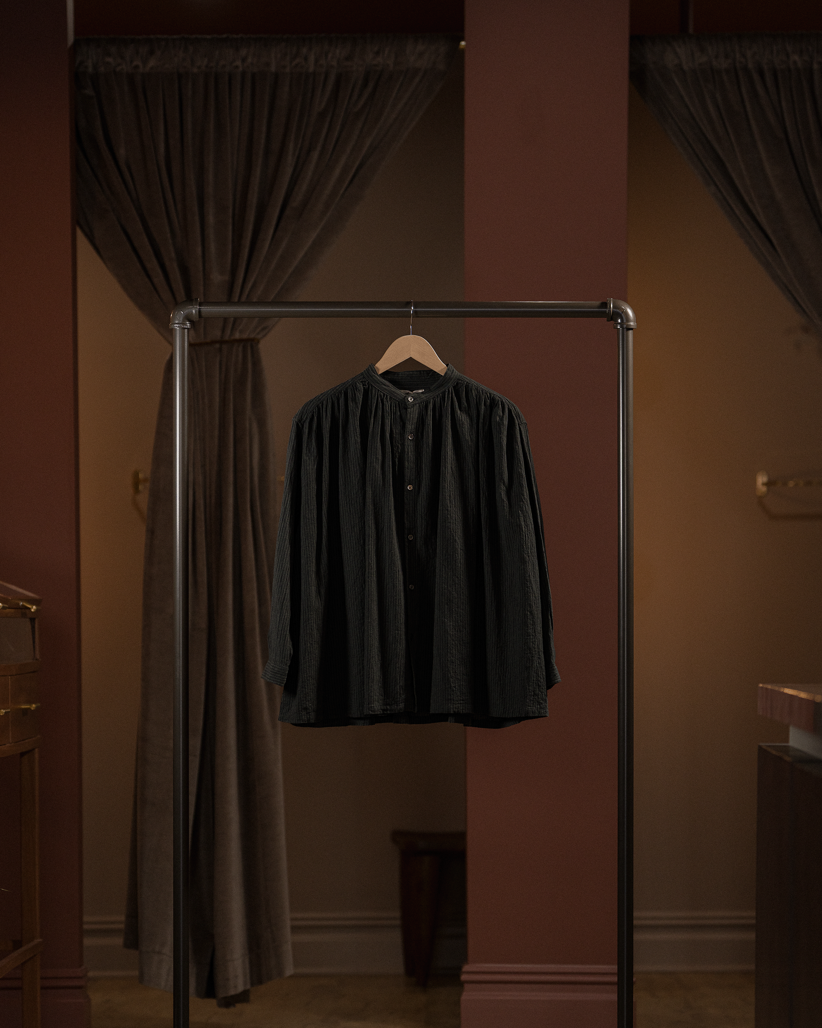 Black shirt hanging on a rack against a brown curtain backdrop