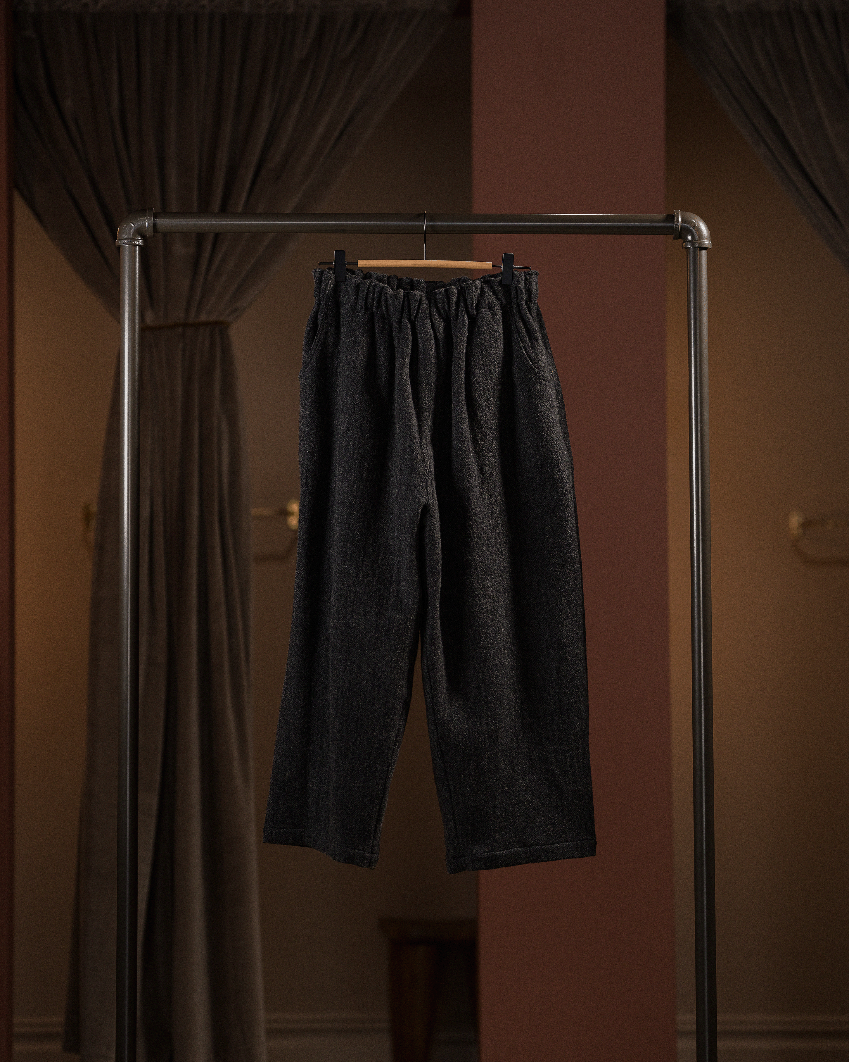 Dark gray pants hanging on a rack against a brown wall.