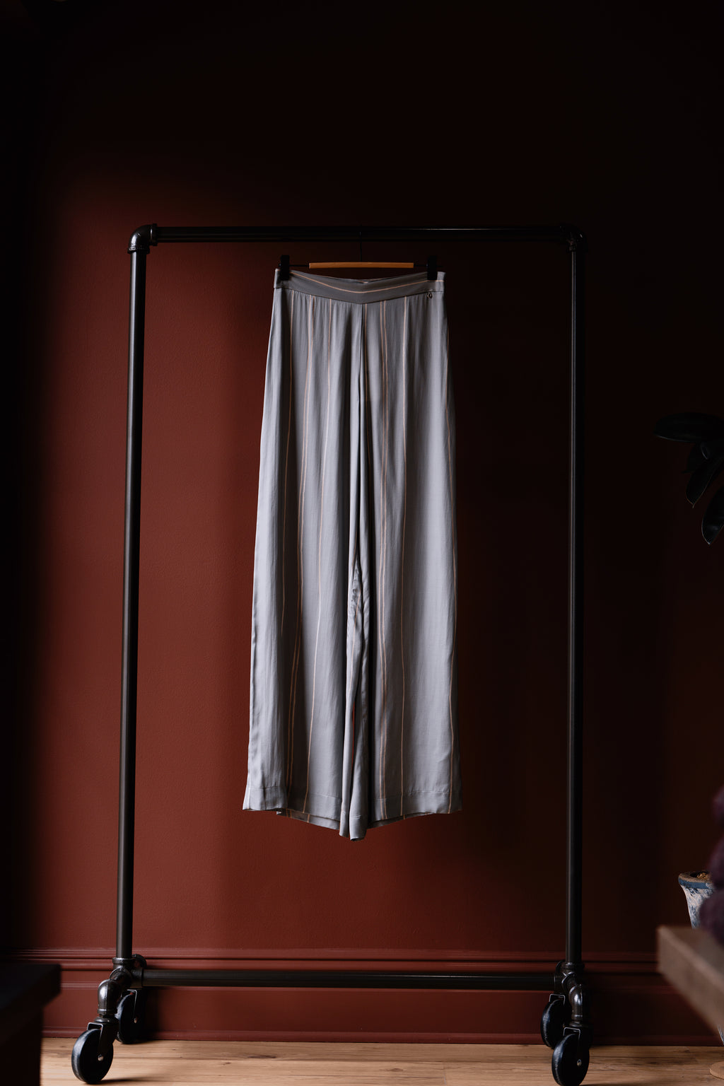 Long gray skirt hanging on a black garment rack against a dark red wall.