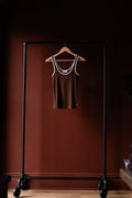 Brown tank top on a hanger attached to a black garment rack against a dark red wall.