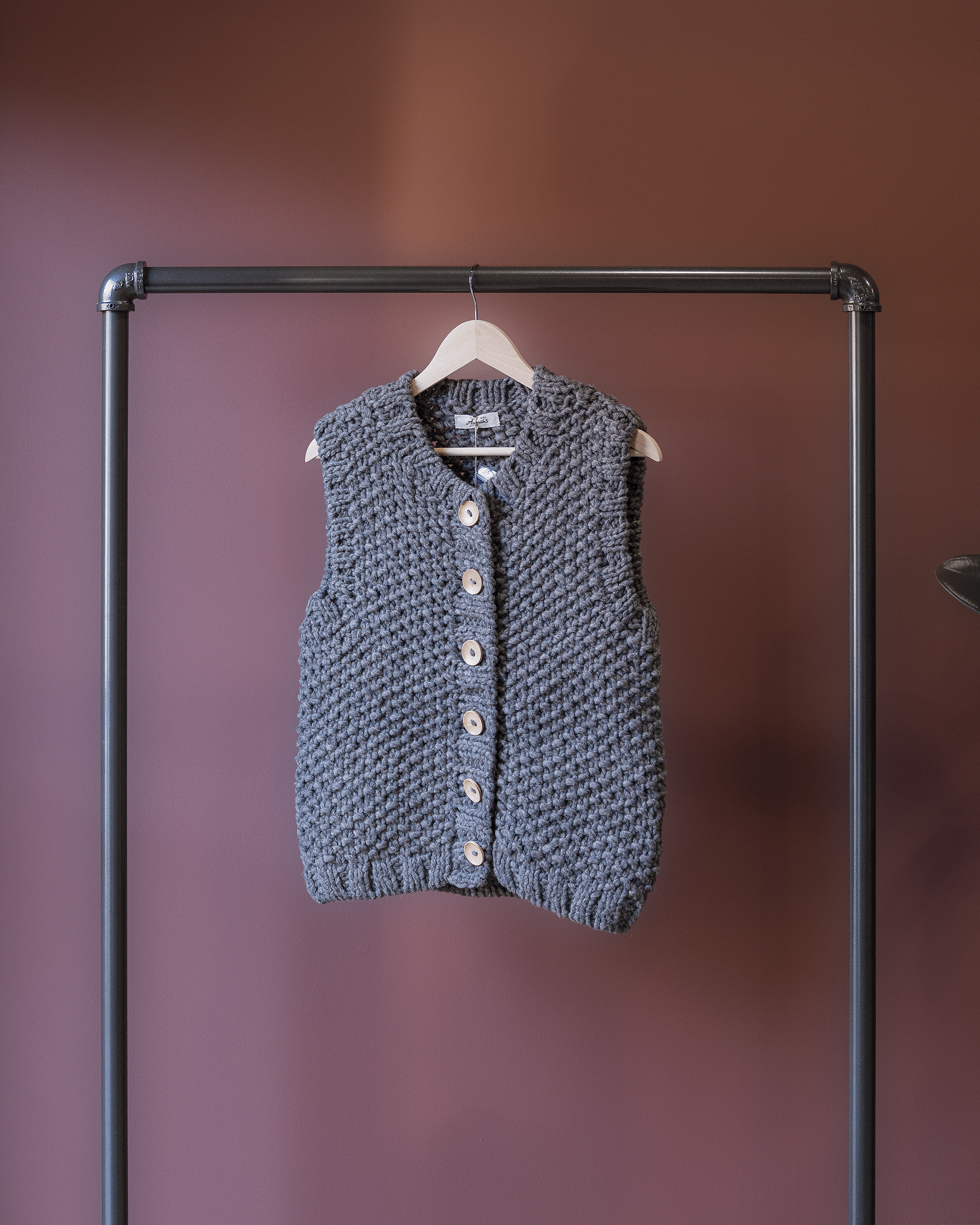 Blue knitted vest on a hanger against a brown background