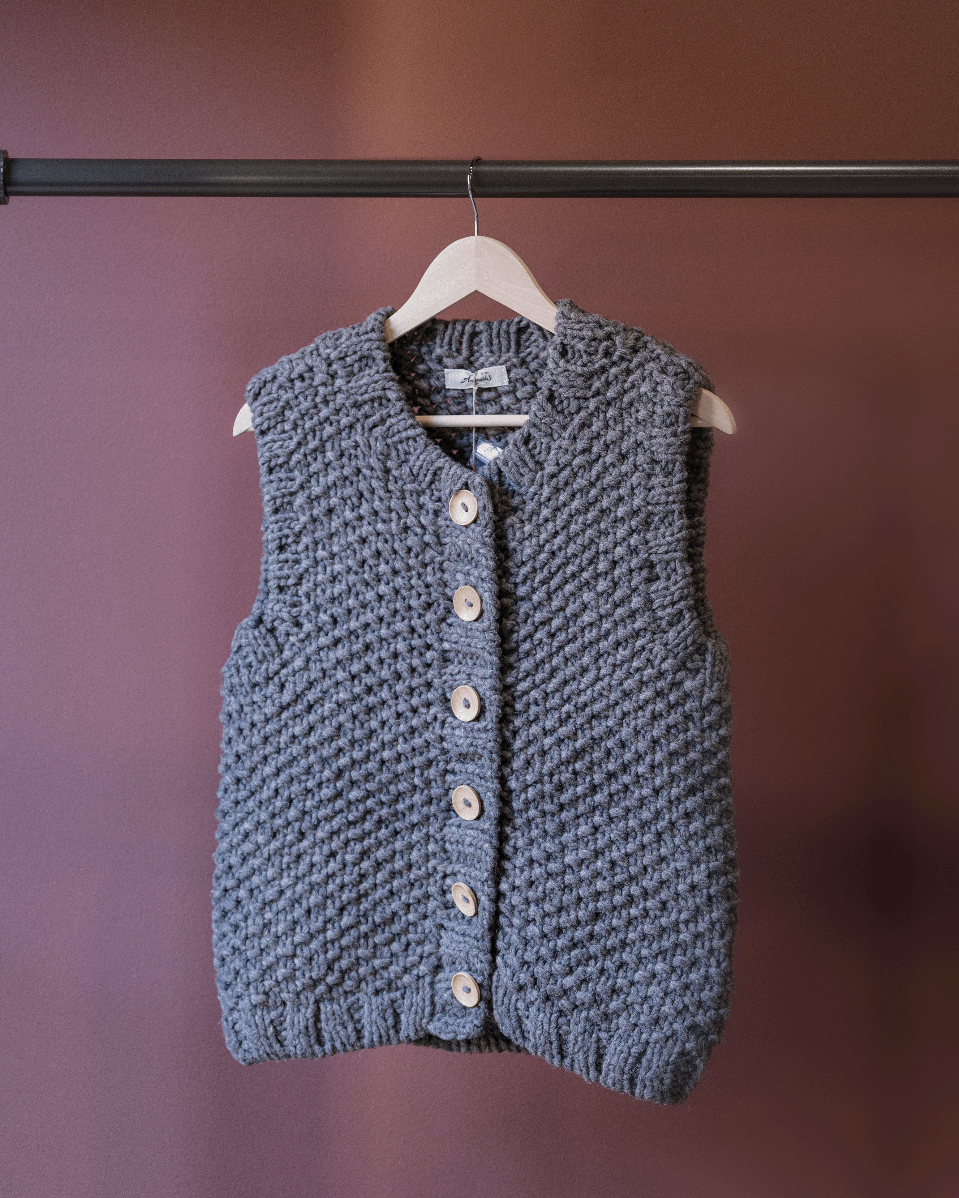 Blue knitted vest on a hanger against a purple background