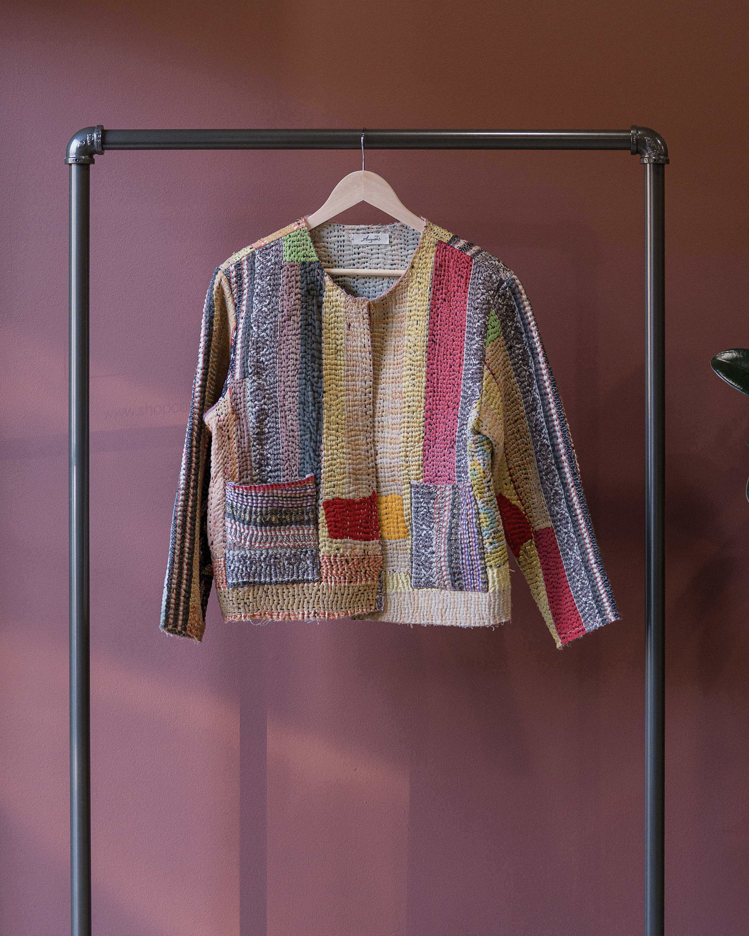 Colorful knitted sweater on a hanger against a pink background