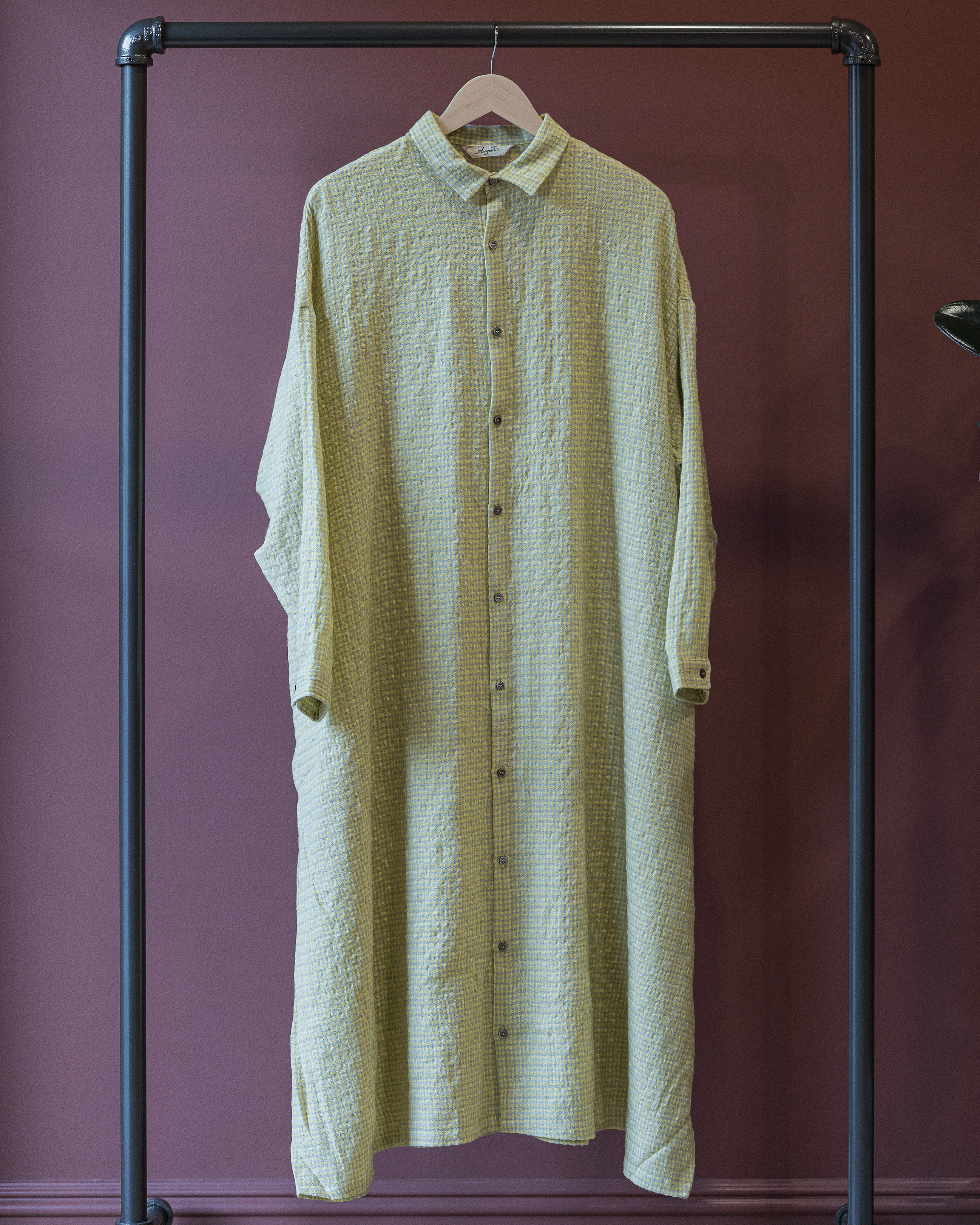 Light green textured dress hanging on a rack against a purple wall