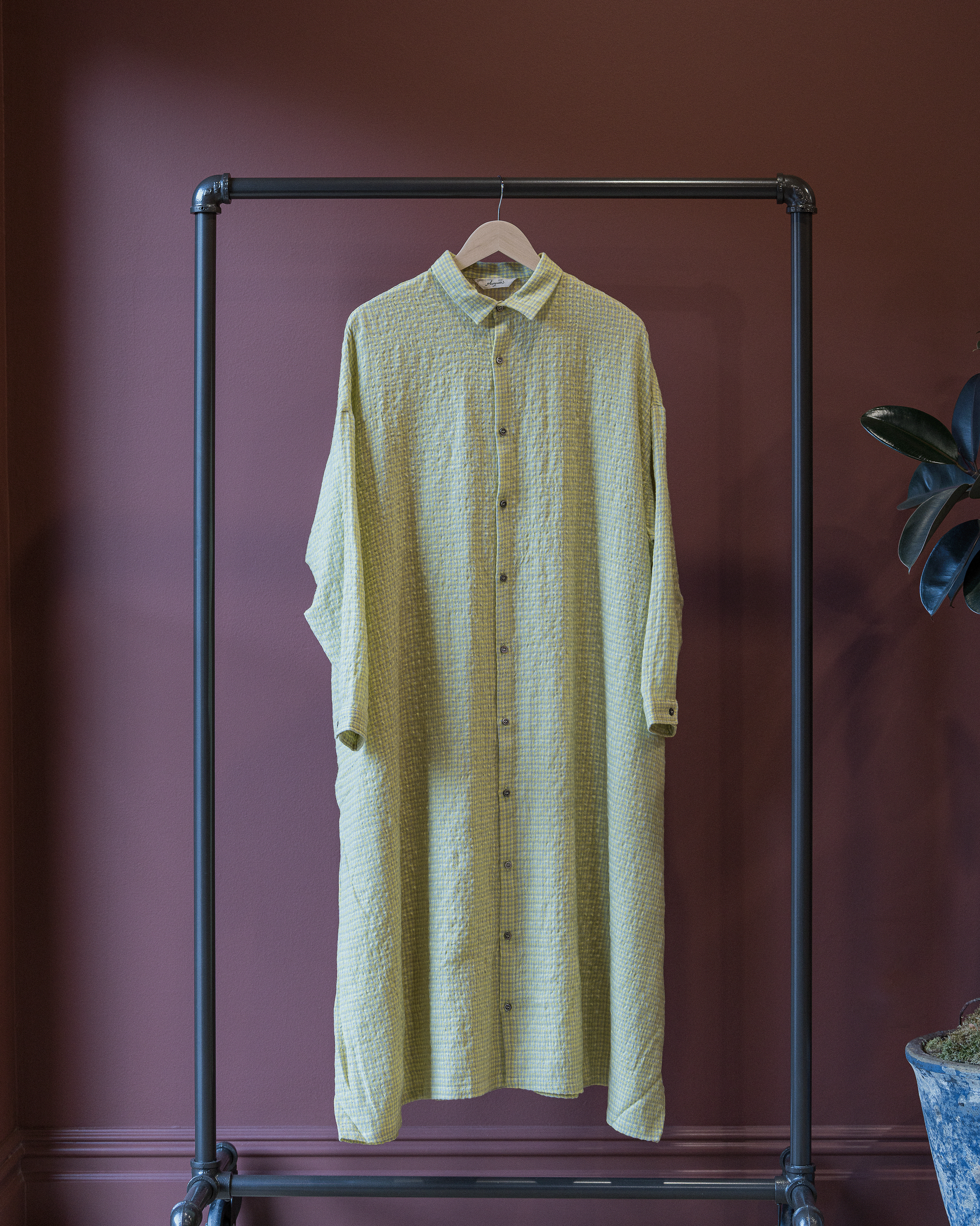 Light green dress hanging on a black metal rack against a dark red wall.
