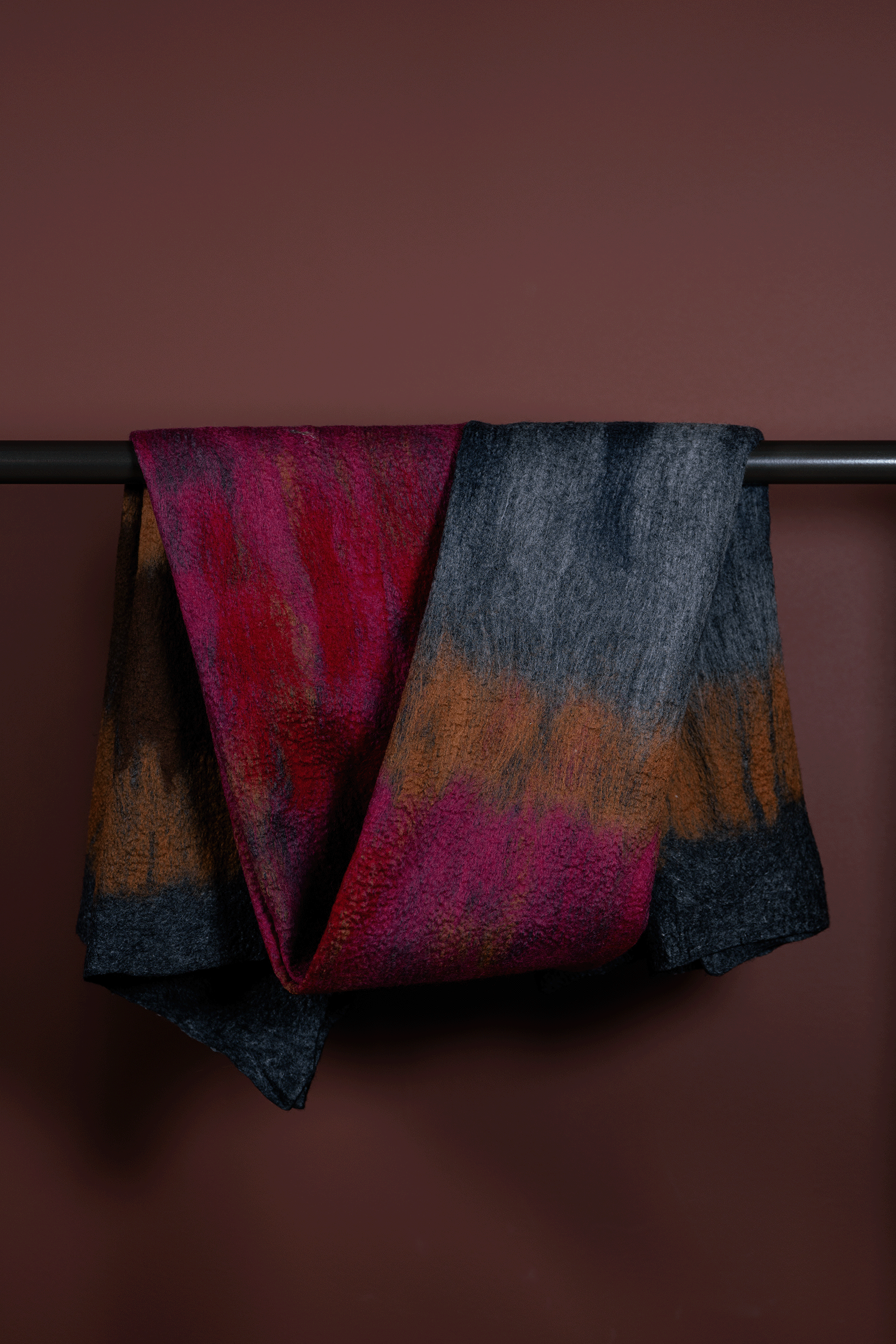 Colorful scarf with a gradient pattern draped over a rod against a brown background