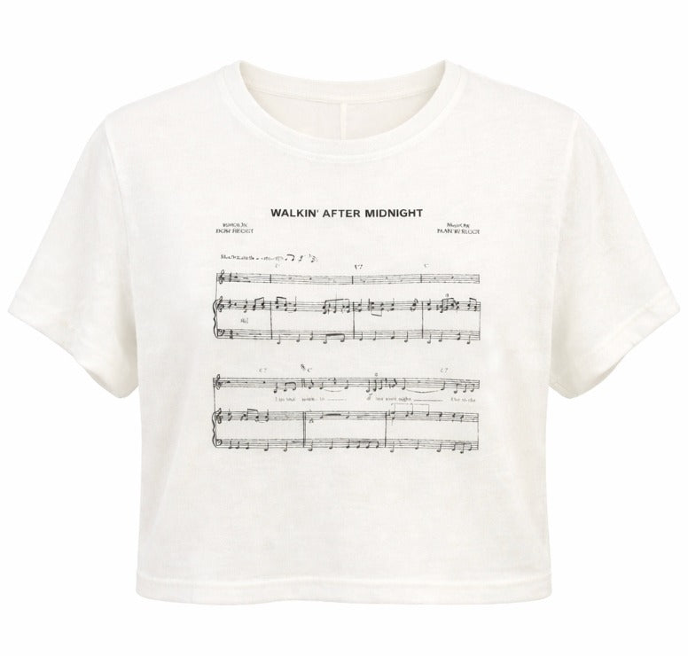 An off-white short-sleeve crop top t-shirt featuring a black printed sheet music graphic with the title 'WALKIN' AFTER MIDNIGHT' on the front. By Fashion Brand Company
