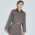 A model wearing a brown and white vertically striped cropped jacket with a brown corduroy collar and a matching striped mini skirt, set against a light gray studio background. Denim Construction Crop Jacket Railroad Stripe by Fashion Brand Company.