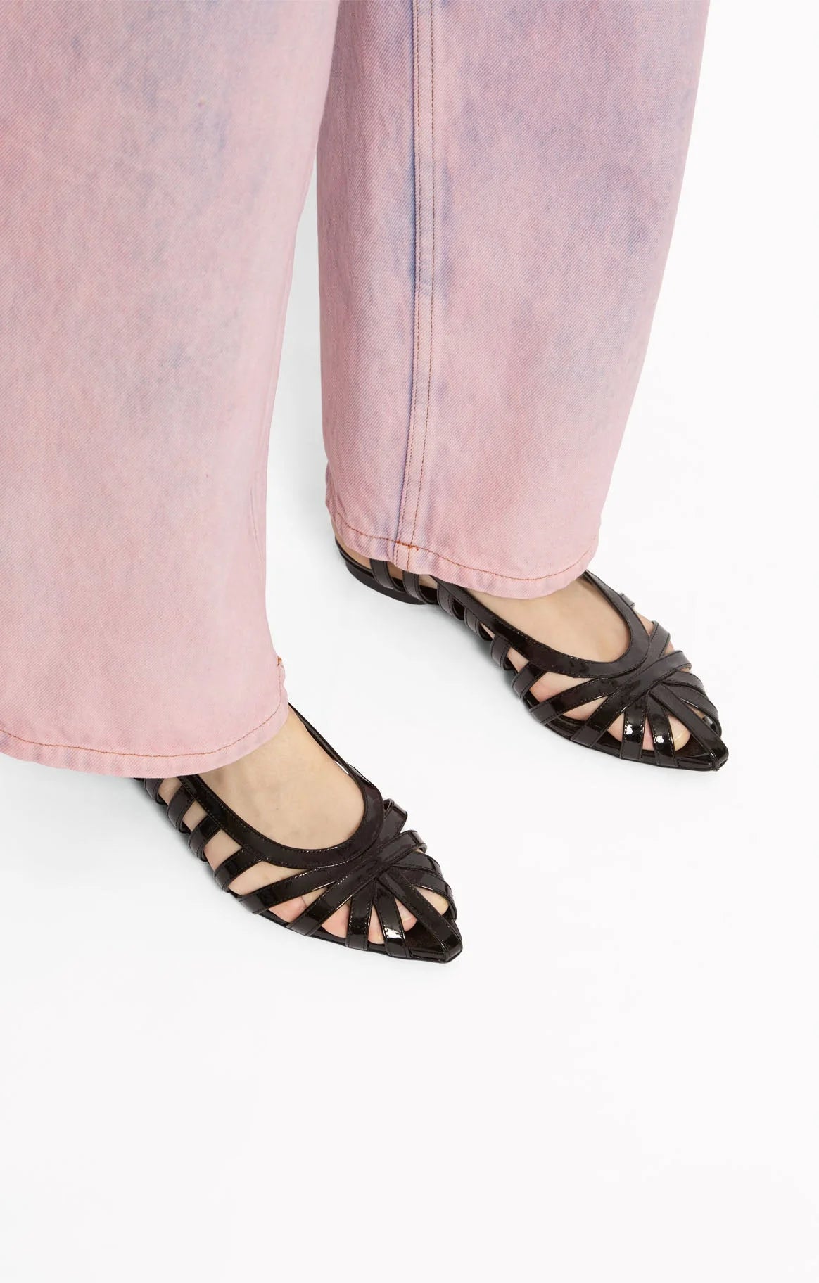Black pointed-toe flats worn with light pink jeans by Roseanna on a white background