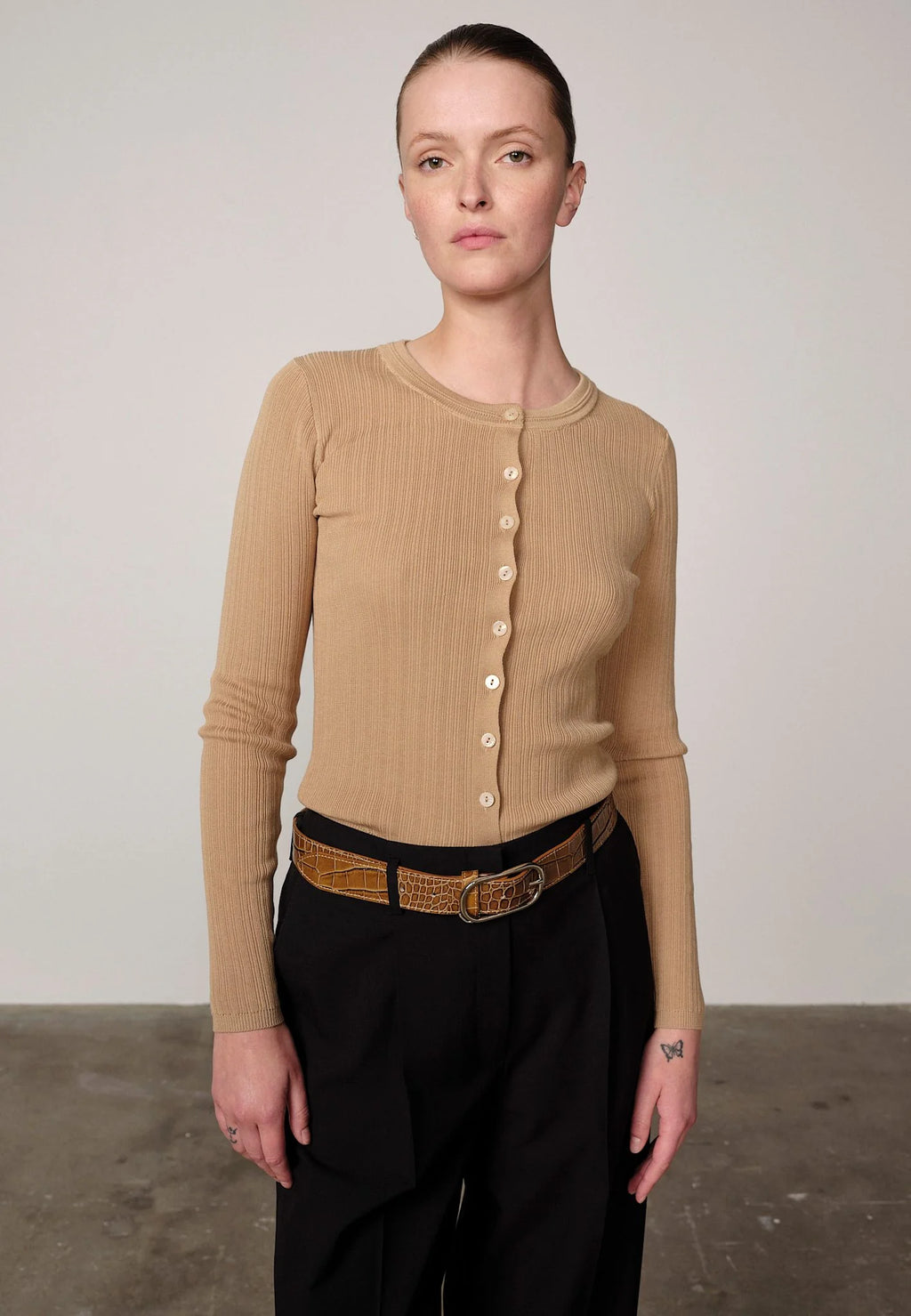 Woman wearing a sand ribbed Brooks sweater blouse by Herskind and black pants against a plain background