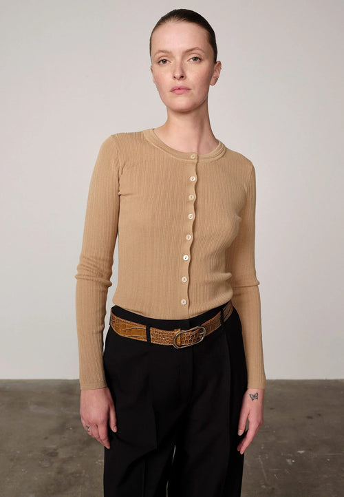 Woman wearing a sand ribbed Brooks sweater blouse by Herskind and black pants against a plain background