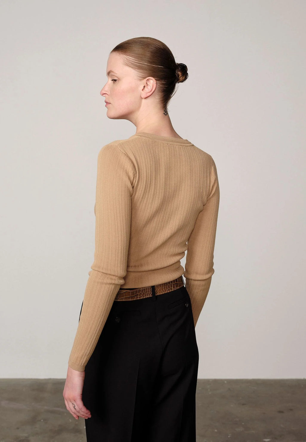 Woman wearing a sand ribbed Brooks sweater blouse by Herskind and black pants against a plain background