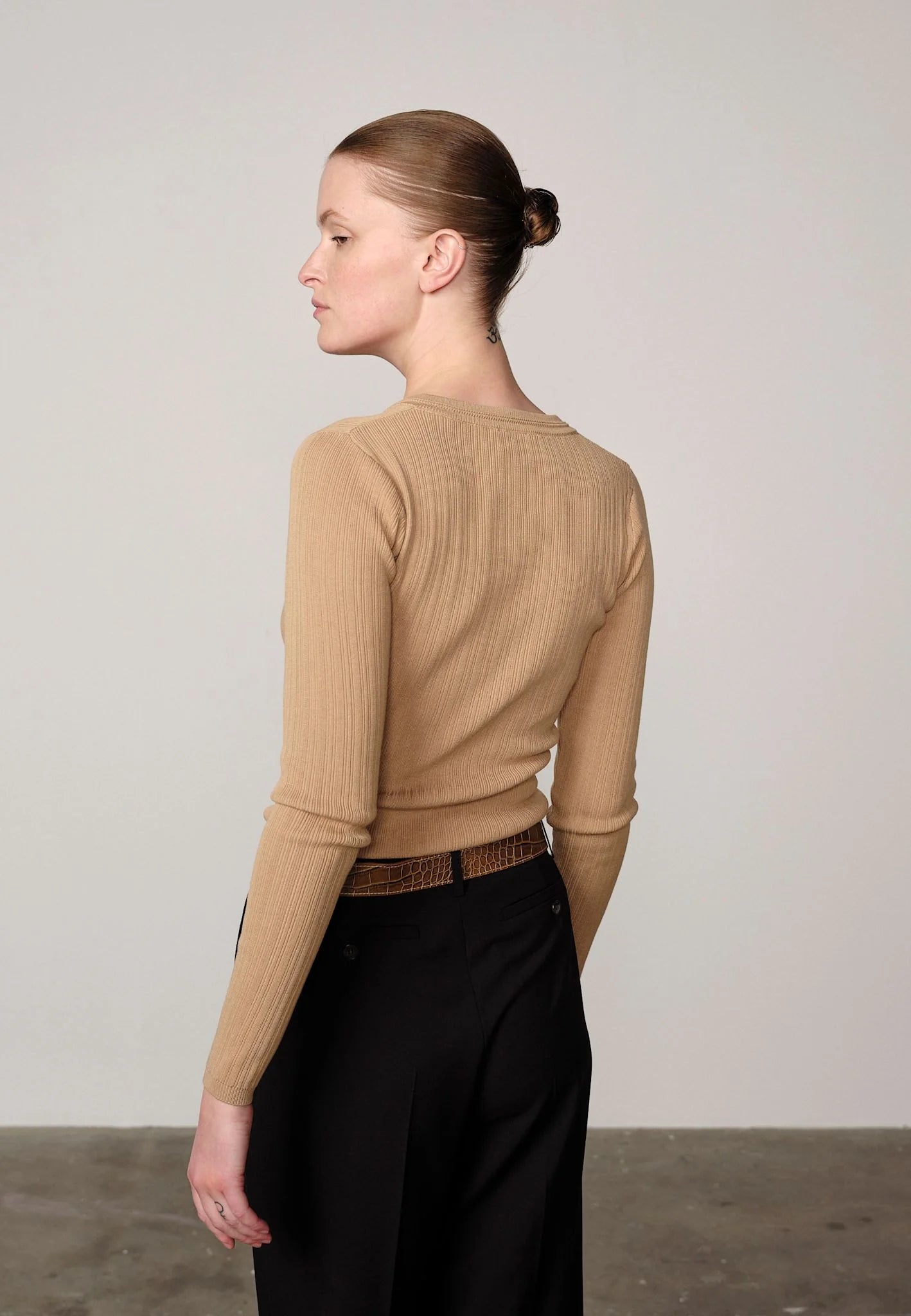 Woman wearing a sand ribbed Brooks sweater blouse by Herskind and black pants against a plain background