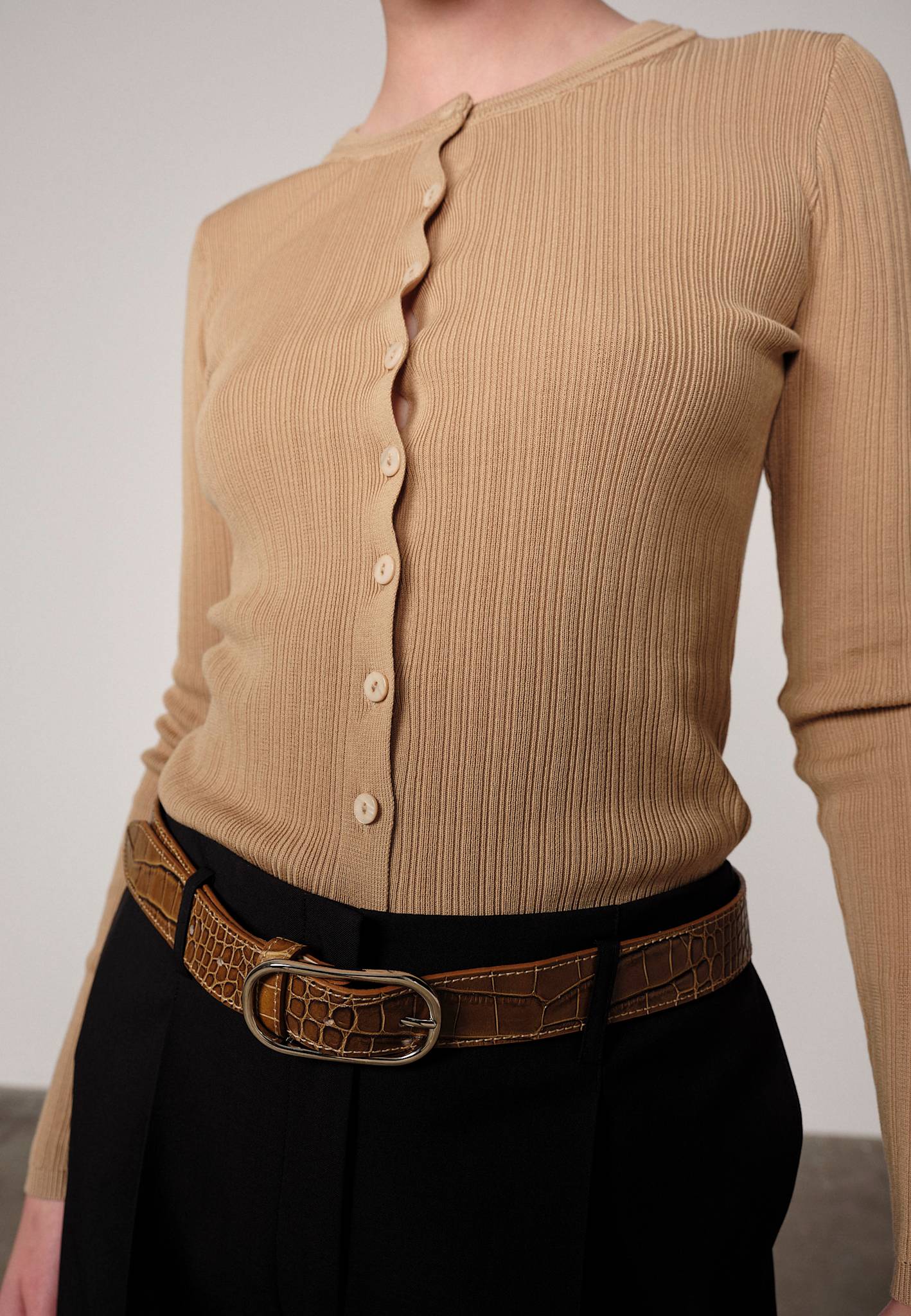 Woman wearing a sand ribbed Brooks sweater blouse by Herskind and black pants against a plain background