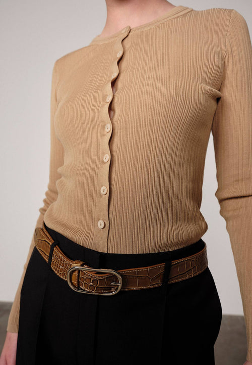 Woman wearing a sand ribbed Brooks sweater blouse by Herskind and black pants against a plain background