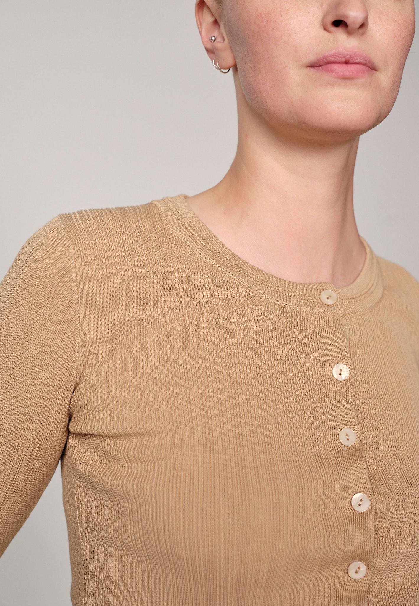 Woman wearing a sand ribbed Brooks sweater blouse by Herskind against a plain background