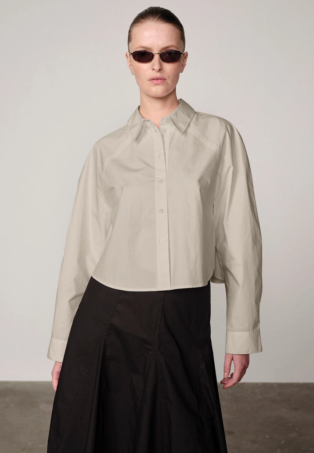 Woman wearing an oyster white Elsie shirt by Herskind and black skirt against a plain background
