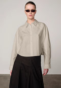 Woman wearing an oyster white Elsie shirt by Herskind and black skirt against a plain background