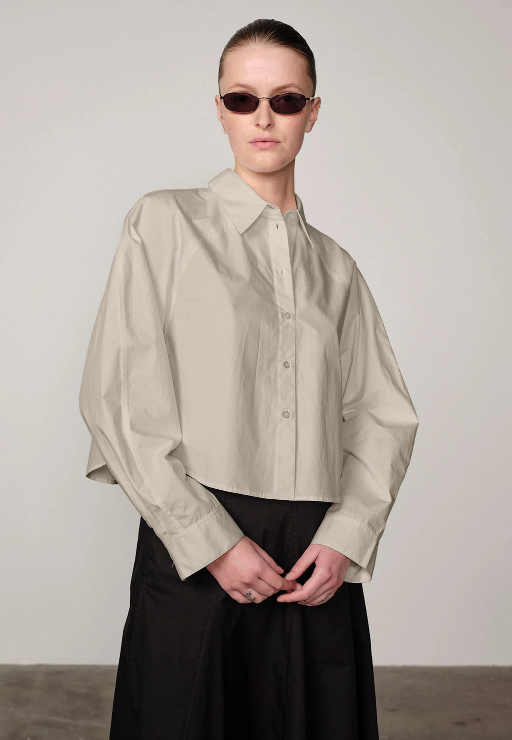 Woman wearing an oyster white Elsie shirt by Herskind and black skirt against a plain background